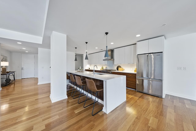 kitchen featuring wall chimney exhaust hood, high end fridge, white cabinetry, light hardwood / wood-style flooring, and pendant lighting