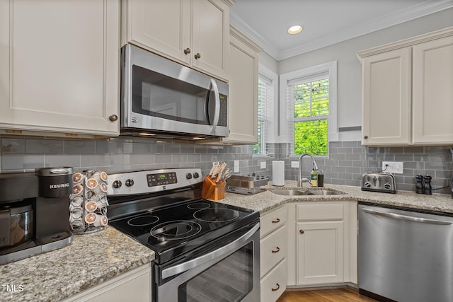 kitchen featuring tasteful backsplash, ornamental molding, light stone counters, stainless steel appliances, and a sink