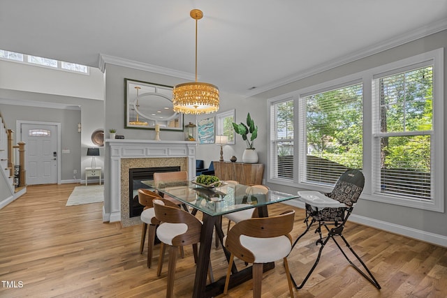 dining space featuring light wood-style flooring, a fireplace, baseboards, and ornamental molding