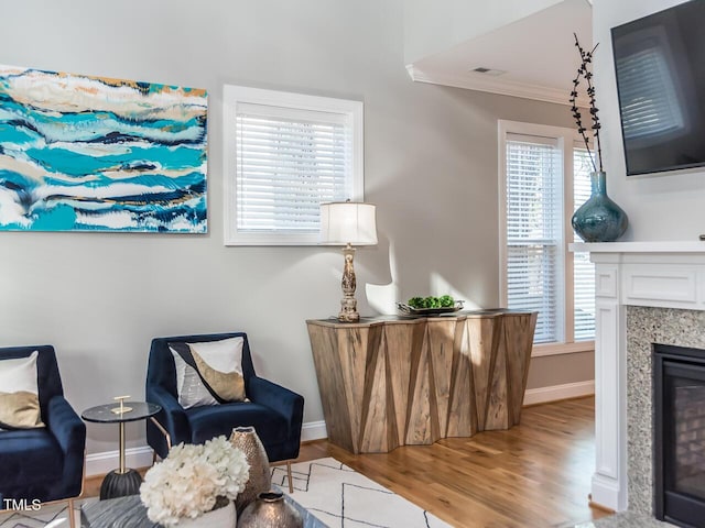 living area featuring visible vents, baseboards, ornamental molding, a fireplace, and wood finished floors