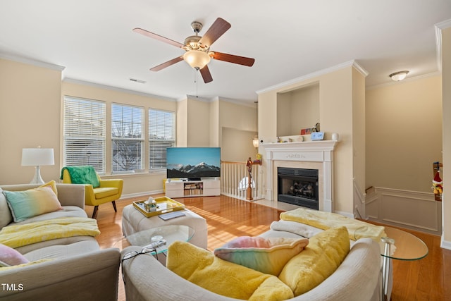 living area with a fireplace with flush hearth, visible vents, wood finished floors, and ornamental molding