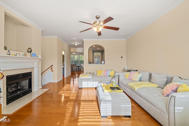 living room with a fireplace, visible vents, light wood-style floors, ornamental molding, and ceiling fan