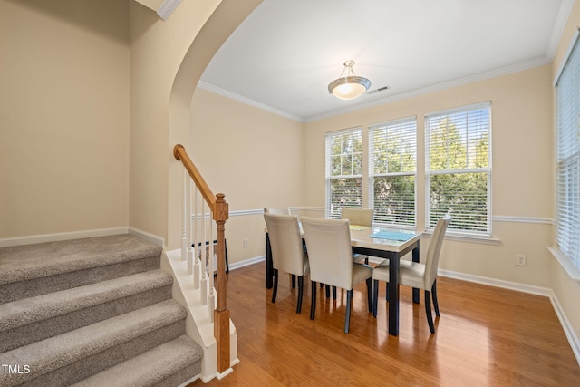 dining space featuring arched walkways, crown molding, light wood finished floors, visible vents, and baseboards