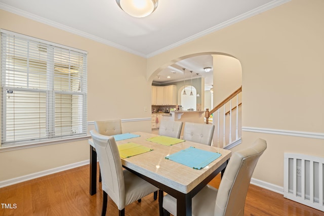 dining room with arched walkways, crown molding, stairway, light wood-style flooring, and baseboards