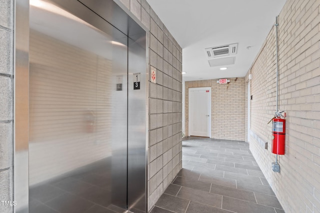 corridor featuring elevator and brick wall