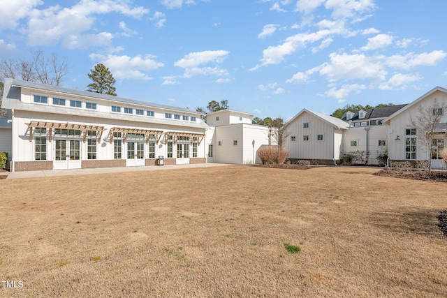 back of house with board and batten siding, a yard, and french doors