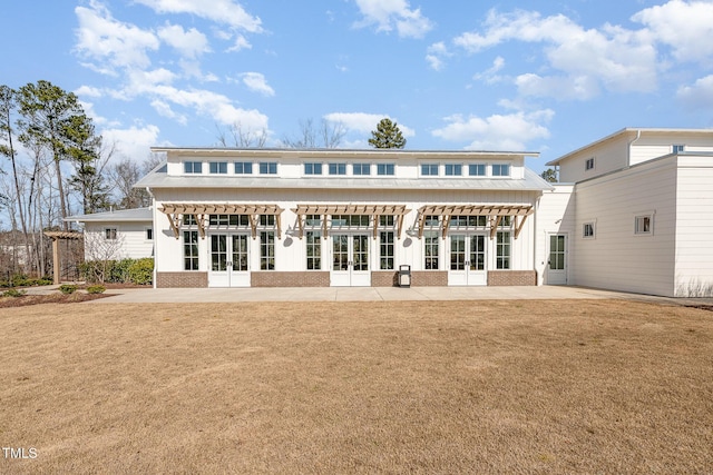 rear view of house featuring brick siding, french doors, a lawn, and a patio area