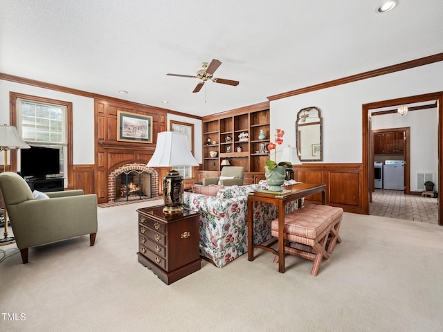 living area featuring light carpet, a wainscoted wall, washing machine and dryer, and ornamental molding