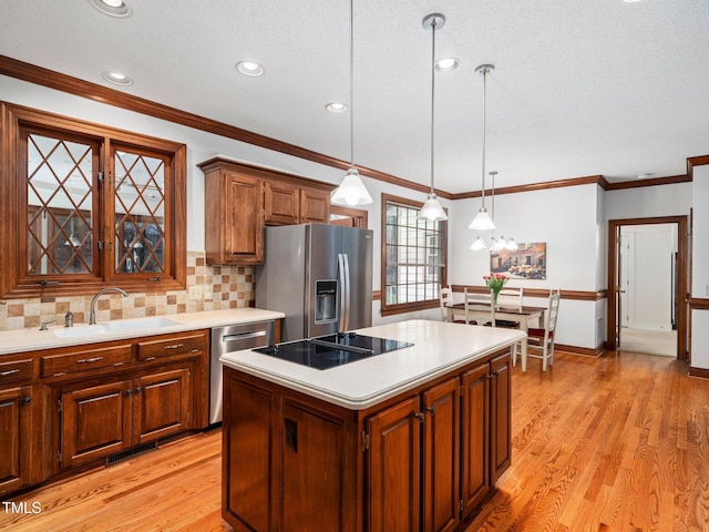 kitchen with stainless steel appliances, a sink, a kitchen island, light countertops, and pendant lighting