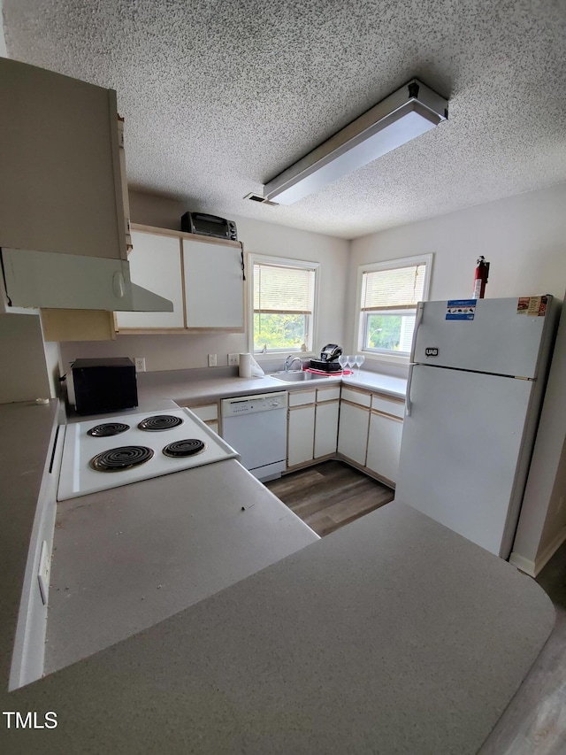 kitchen with white appliances, light countertops, a textured ceiling, white cabinetry, and a sink