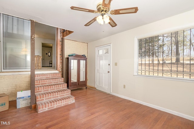 foyer entrance with brick wall, baseboards, ceiling fan, and wood finished floors