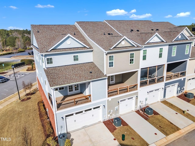 view of front of property featuring cooling unit, a garage, driveway, roof with shingles, and a residential view