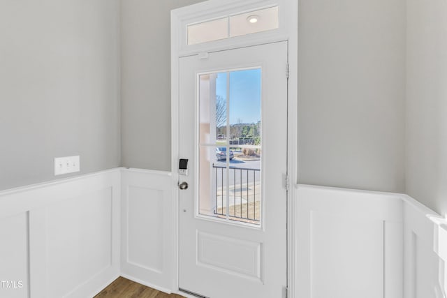 doorway to outside featuring a wainscoted wall, wood finished floors, and a decorative wall