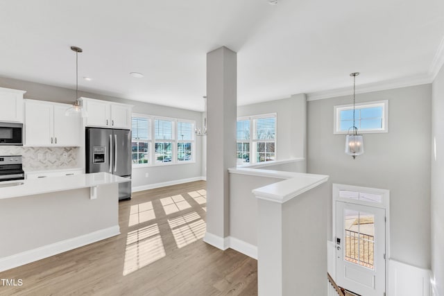 kitchen with decorative light fixtures, light countertops, light wood-style flooring, appliances with stainless steel finishes, and white cabinets