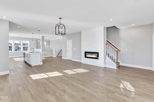 unfurnished living room with a notable chandelier, recessed lighting, a sink, and light wood-style floors