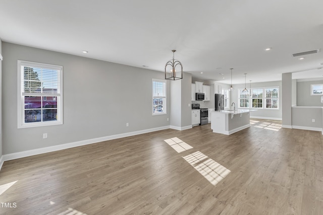 unfurnished living room featuring a chandelier, light wood-style flooring, recessed lighting, visible vents, and baseboards