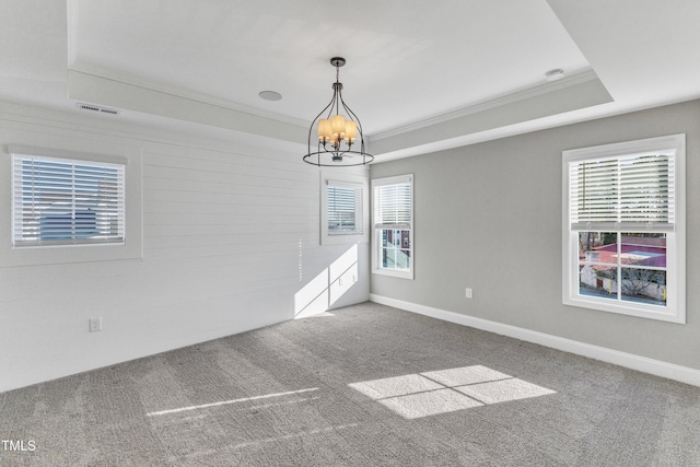 carpeted spare room featuring ornamental molding, a wealth of natural light, a raised ceiling, and a notable chandelier