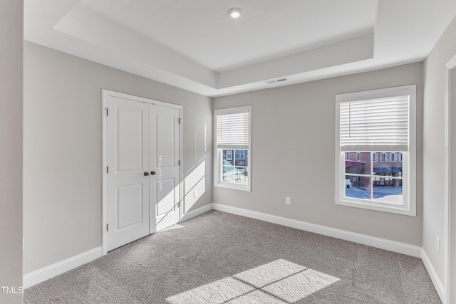 unfurnished bedroom with light carpet, baseboards, and a raised ceiling