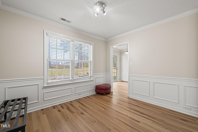 empty room with crown molding, wainscoting, visible vents, and light wood-style floors