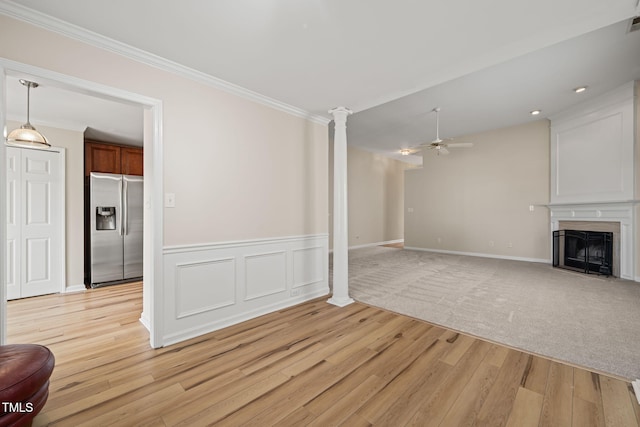 unfurnished living room with a fireplace with flush hearth, ceiling fan, ornate columns, and ornamental molding