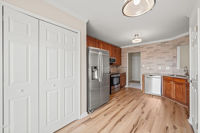 kitchen featuring stainless steel appliances, brown cabinetry, a sink, and ornamental molding