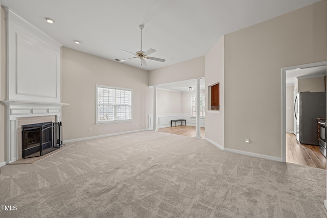 unfurnished living room with light carpet, a large fireplace, ceiling fan, and ornate columns