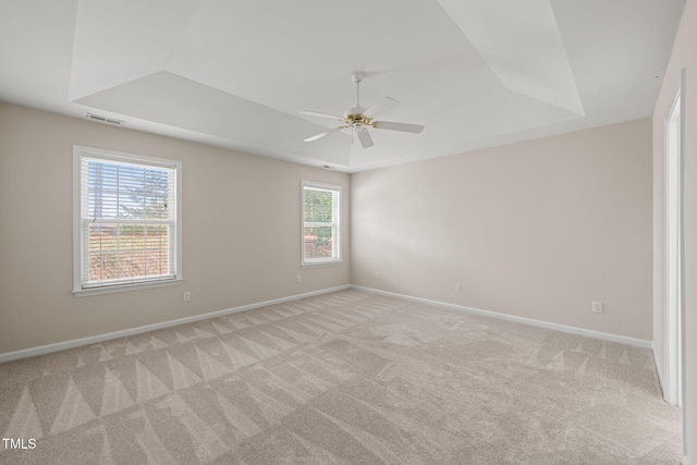 empty room with a raised ceiling, light colored carpet, visible vents, a ceiling fan, and baseboards