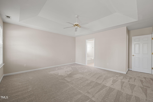 carpeted spare room with a tray ceiling, visible vents, ceiling fan, and baseboards