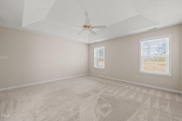 carpeted empty room featuring visible vents, baseboards, a raised ceiling, and a ceiling fan