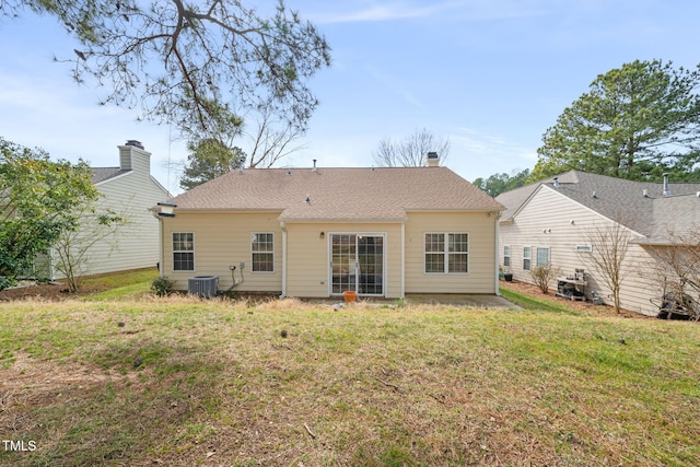 rear view of house with central AC, roof with shingles, and a lawn