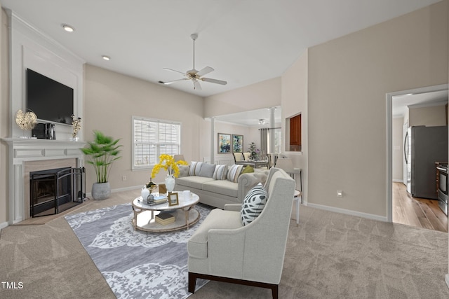 living area featuring light carpet, a fireplace, baseboards, and a ceiling fan