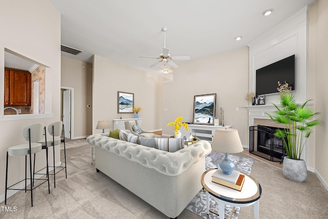 living area featuring light carpet, baseboards, visible vents, a ceiling fan, and a glass covered fireplace