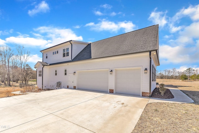 view of side of property with concrete driveway, roof with shingles, and an attached garage