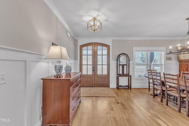 foyer entrance with arched walkways, french doors, crown molding, an inviting chandelier, and light wood-style floors