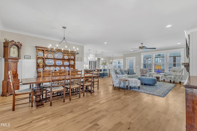 dining space featuring a decorative wall, ornamental molding, wainscoting, light wood-type flooring, and ceiling fan with notable chandelier