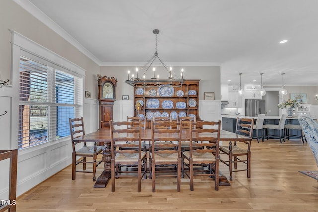 dining room with a chandelier, a decorative wall, light wood-style floors, ornamental molding, and wainscoting