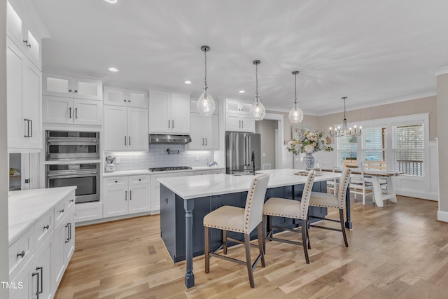 kitchen with appliances with stainless steel finishes, glass insert cabinets, white cabinets, an island with sink, and under cabinet range hood