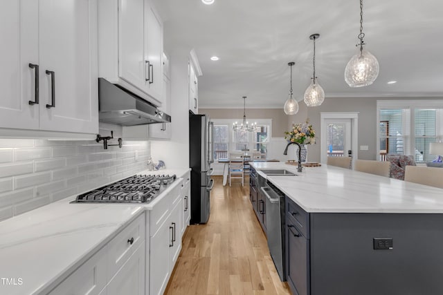 kitchen featuring decorative light fixtures, white cabinets, a large island with sink, and under cabinet range hood