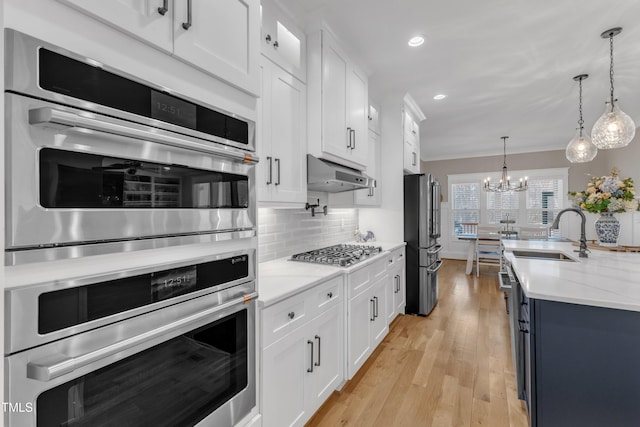 kitchen featuring under cabinet range hood, stainless steel appliances, a sink, white cabinets, and decorative light fixtures