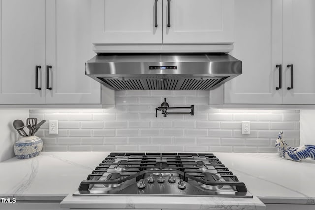 room details with stainless steel gas cooktop, extractor fan, white cabinets, and light stone countertops