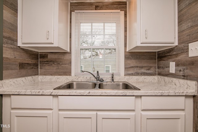 kitchen featuring white cabinetry, sink, and wood walls