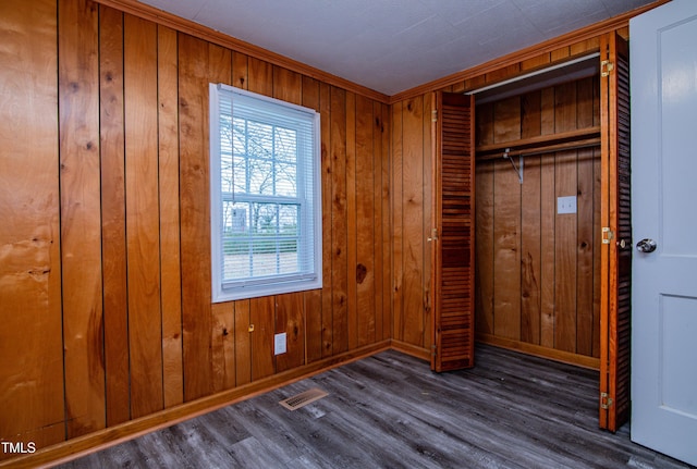 unfurnished bedroom featuring dark wood-type flooring, wooden walls, and a closet