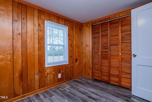 unfurnished bedroom featuring dark hardwood / wood-style flooring, a closet, and wood walls