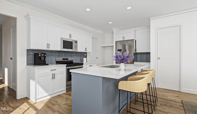 kitchen with appliances with stainless steel finishes, white cabinets, a kitchen breakfast bar, ornamental molding, and a kitchen island with sink