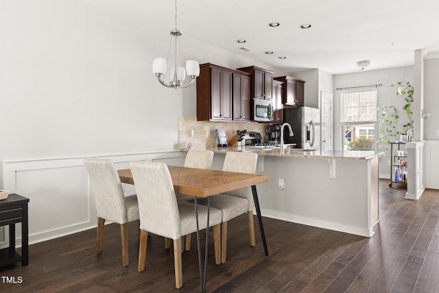 kitchen with hanging light fixtures, appliances with stainless steel finishes, dark hardwood / wood-style floors, light stone countertops, and backsplash