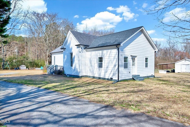 view of side of home featuring entry steps, roof with shingles, and a lawn