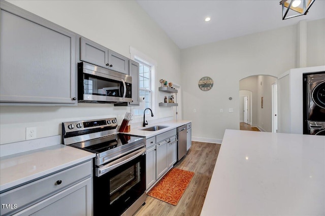 kitchen with stacked washer / drying machine, light countertops, appliances with stainless steel finishes, gray cabinets, and open shelves