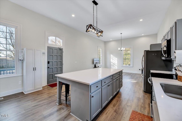 kitchen featuring appliances with stainless steel finishes, a center island, hanging light fixtures, light countertops, and gray cabinetry