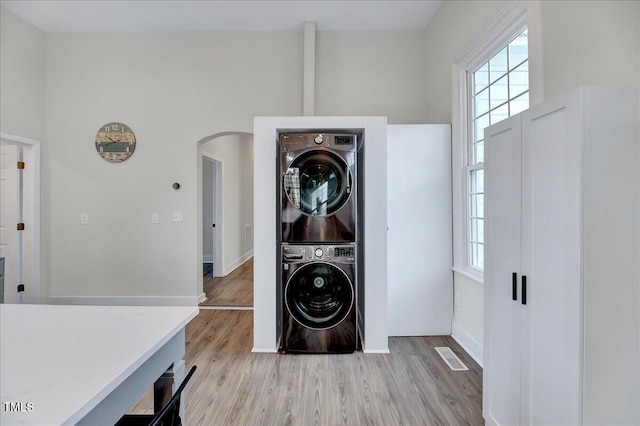 laundry area with stacked washing maching and dryer, laundry area, arched walkways, and light wood-style floors