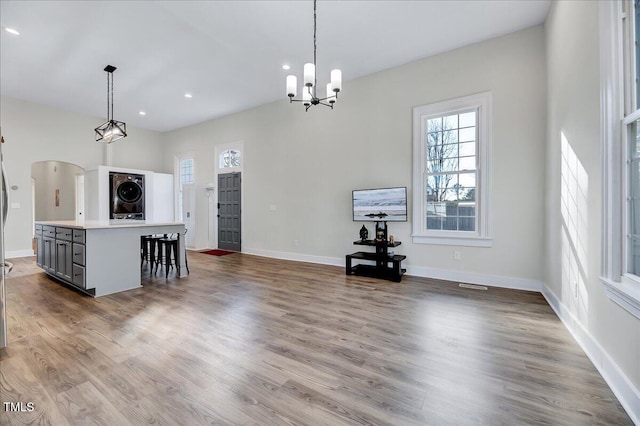 interior space featuring baseboards, arched walkways, stacked washer / drying machine, and wood finished floors